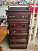 Front view of antique dark wood dresser with five drawers, showing metal pulls and keyhole accents.