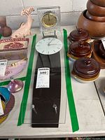 Full lot with Howard Miller wall clock laid flat with curved dark wood and white clock face in front, Sasaki crystal clock behind, surrounded by other household items