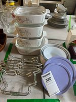 Stacked four Corningware casseroles with clear glass lids and floral iris pattern, three storage containers with mismatched lids, metal racks