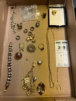 Overview of costume jewelry assortment including bracelets, rings, pins, and necklaces arranged in a box.