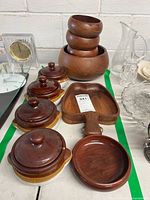 Four lidded crocks in brown and tan glaze, wooden salad set with nested bowls and salad servers on table