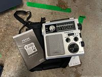 Eton FR-300 radio, carrying case, and user manual laid out, showing front and sides of radio and manual cover.