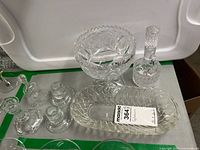 Photo showing multiple clear glass pieces including cruet, candle sticks, bell, serving dish, and decorative bowl.