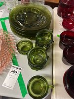 Green glass luncheon plates stacked with cups on a white table, showing the raised dot detail on the edges.