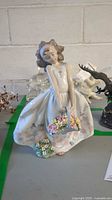Full front view of the Lladro girl figurine holding basket of flowers, showing the flowing dress and hair detail.