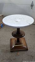 Marble top side table with round white marble top and wooden pedestal base with square bottom.