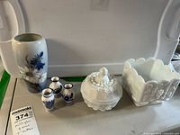 Lot includes a Royal Copenhagen tall vase with floral design, three blue and white miniature vases, a white milk glass lidded dish with grape motif, and a white milk glass square planter with grapevine relief and scalloped edges.