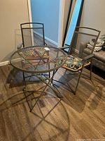 Two metal folding chairs with mesh design and colorful tropical leaf pattern cushions, showing rust on metal frames.