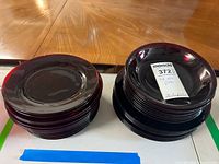 Two stacks of red glass plates and bowls on a wooden table; the left stack consists of smaller bowls and the right stack of plates, all have a deep red color with smooth glossy finish.
