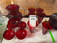 Red glass pitcher, four red footed glasses, and six small red footed bowls arranged on a table.