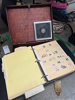 Wooden box open showing framed coin and ring binder with stamps inside.