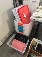 Stacked clear plastic storage bins with various colored lids (red, black, pink) shown from side angle.