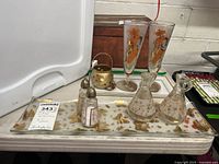 Full view of lot items on large tray showing two tall decorated glasses, cruets, salt and pepper shakers, two trays, and small gold container.