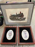 Overview of all three framed art pieces: one larger original painting of a building, two smaller framed enameled porcelain oval plaques with figurative artwork