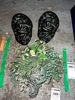 Photo showing two black hollow cast metal wall shelves with relief figures and one resin wall pocket with assorted faux greenery.