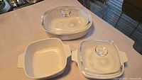 Three casserole dishes displayed: plain white oval with lid, plain white square without lid, Blue Cornflower square with lid