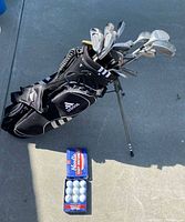 Full view of Adidas stand bag loaded with clubs and box of golf balls on ground