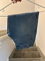 Blue denim jeans folded over hanger, rear pocket visible