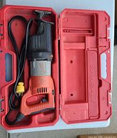 Saw with cord placed inside open red carrying case