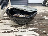 Ceramic basin with stone cover partially lifted, showing interior pebbles and cable