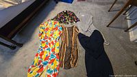 Five garments laid out: colourful sequin jacket, grey cardigan, floral dress, brown tribal dress, navy dress