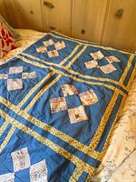 Full view of the antique quilt laid out on a bed, showing patchwork blocks with blue background and yellow borders.