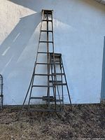 Front view of three antique wooden ladders leaning against an outdoor white wall, showing overall worn condition and size differences