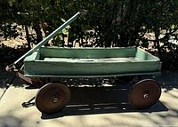 Side view of the antique wooden wagon showing the green wood body and metal wheels.