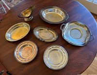 Full lot of silver plate serving pieces arranged on wooden table, including platters, bowls, dishes, and gravy boat