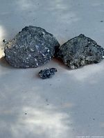 Three galena and silver ore mineral specimens arranged on a flat surface, showing their metallic and crystalline textures.
