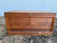 Front view of the wooden blanket chest showing rectangular shape, flat lid, latch, wood grain and surface wear