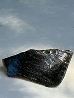 Side view of the black obsidian rock showing its glossy texture and sharp edges under diffuse light.
