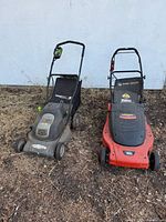 Photo showing two electric lawn mowers on a dirt ground against a white wall; one is gray and green Earthwise, the other is red and black Black & Decker