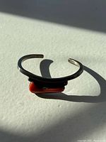 Front angled view of vintage sterling silver bracelet with red coral stone centerpiece casting shadow on surface