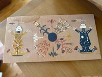 Full view of the sand painting showing two stylized figures and central symbolic elements.