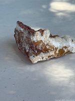 Side angle close-up of the raw selenite crystal showing white crystalline surfaces and brown matrix base on a light background.