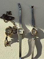 Three vintage ladies watches laid out on a flat surface in sunlight showing overall lot condition and item types.