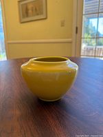 Front view showing the full rounded shape and glossy yellow glaze of the vase on wooden table.