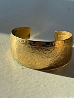 Brass cuff bracelet side view showing engraved figures and geometric border.