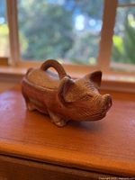 Side view of a rustic brown ceramic pig figurine with a handle formed by a removable lid on its back.