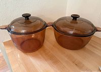 Two large amber-colored glass pots with matching lids on a wooden surface.
