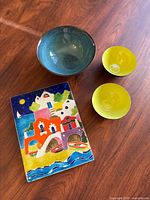 Photo of the ceramic tile and three bowls on wooden surface, showing color and condition.