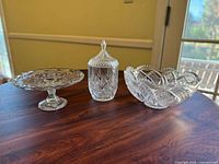 Photo showing the vintage crystal cake stand, covered candy dish, and decorative bowl on a wood surface under natural light.