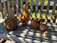 Photo of all items on wooden bench showing metal duck watering can, terracotta owl planter, chicken, cat, and small bird figurines
