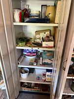 Front view of vintage white metal garage cabinet with doors open showing four shelves filled with assorted vintage household and kitchen items.