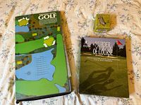 Full view of Thinking Man's Golf game, Murder of Course puzzle box, and Dog Tail Ball Marker box on floral sheet.