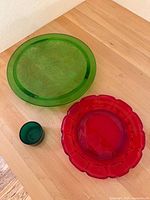 Large green glass tray with floral etching, red glass plate with scalloped rim, small dark green glass cup on wooden surface