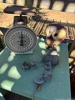 Photo showing the vintage Hanson mechanical scale, metal owl decor, and metal bird wind chime on a green outdoor surface with shadows.