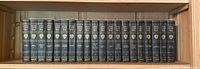 Front view of the full set of 20 Harvard Classics Shelf of Fiction volumes on a wooden shelf, showing uniform blue covers with gold text and insignia on spines.