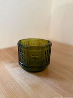 Side angle photo showing the octagonal green glass planter bowl with embossed Aztec pattern on wood surface.